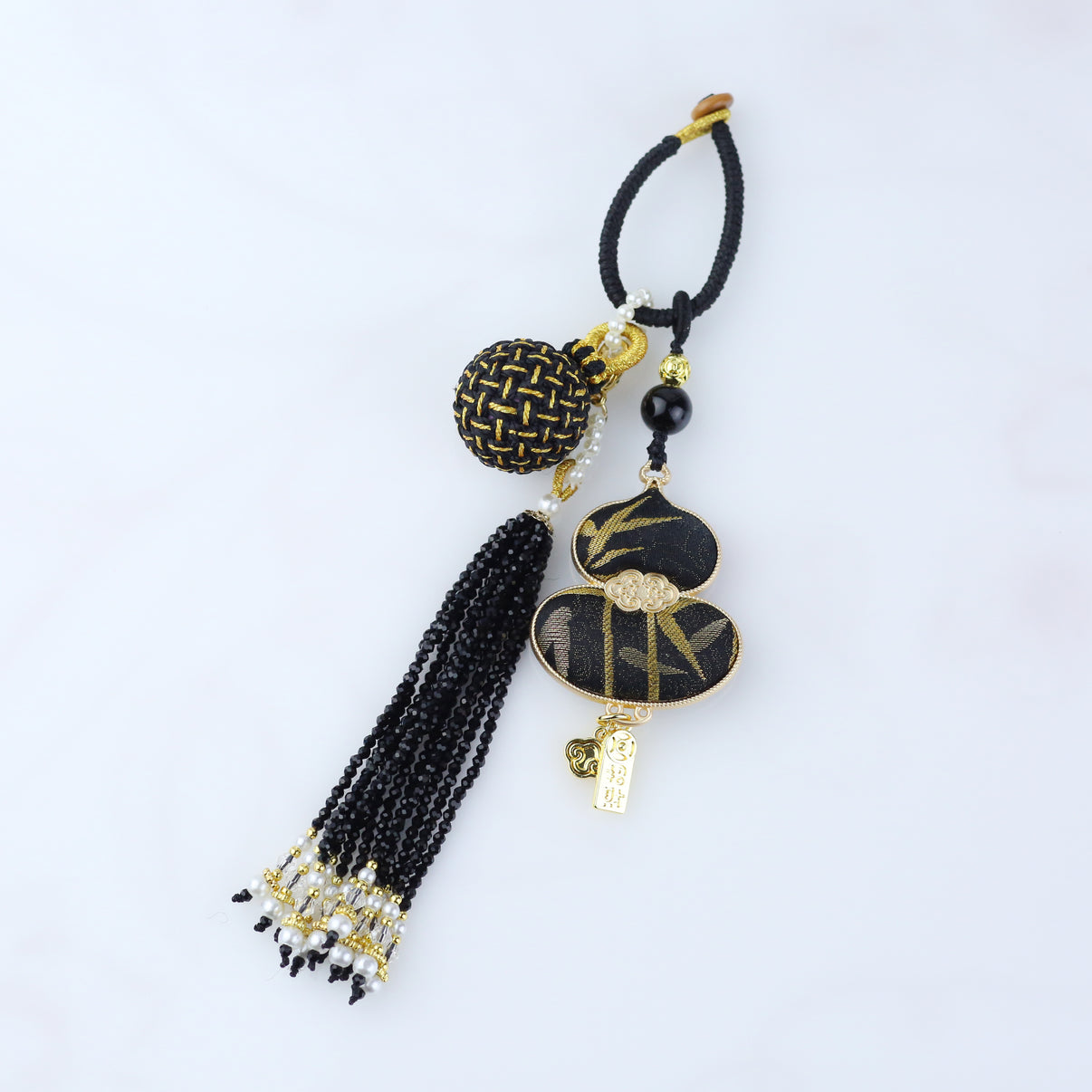 Close-up of handmade black-and-gold Song brocade feng shui gourd pendant showing embroidery and metal details.